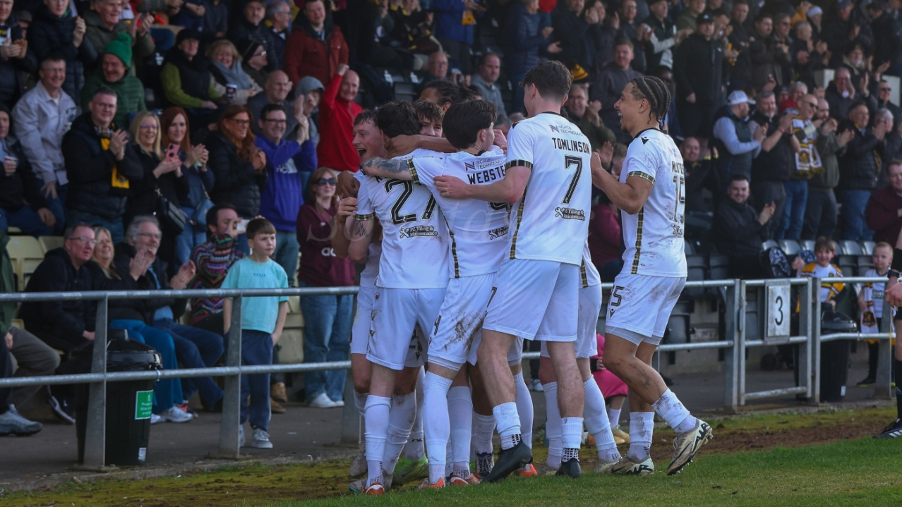 Dumbarton players celebrate a goal in front of a packed stand